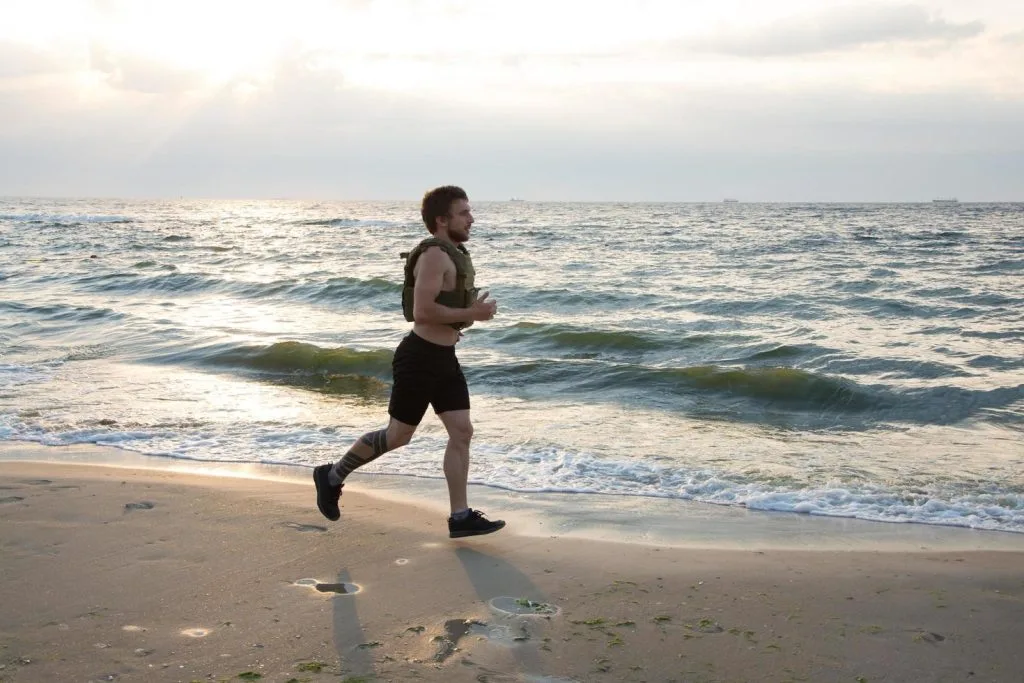 Jeune athlète barbu en train de faire un exercice avec un gilet lesté pour améliorer sa force et son endurance.